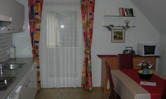 A cozy kitchen with a dining area. The windows have colorful curtains, and there is a table with chairs.