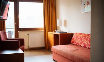 A cozy room with a red sofa and a comfortable armchair. A large window with curtains provides plenty of daylight.