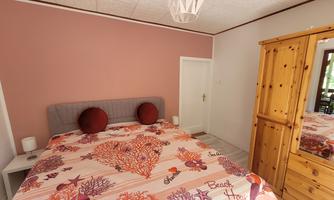 A cozy bedroom with a large bed and colorful bedding. There is a wooden closet against the wall, and the room has a warm color scheme.