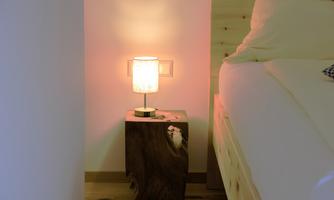 A cozy bedroom area with a wooden nightstand and an elegant lamp. The soft lighting creates a relaxed atmosphere.