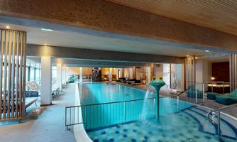 A modern indoor pool with a blue water surface. Relaxing loungers and a bright, inviting atmosphere are visible.
