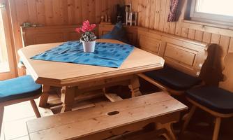A cozy dining area with a wooden table and benches. On the table is a blue table runner and a flower in a pot.