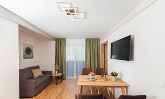 A modern living room with a cozy sofa and a dining table. Large windows with curtains let in plenty of light.