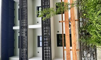 A modern building with three floors and balconies. In front of the house is a wooden fence and green plants.