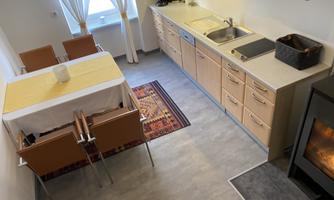 A modern kitchen with a table and chairs. Next to the kitchenette is a small oven, and the room has plenty of daylight.