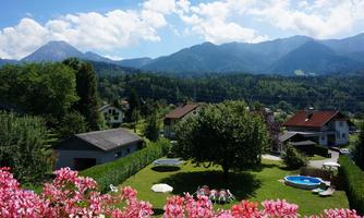 A tranquil landscape with flowers in the foreground and a well-kept garden. In the background, majestic mountains rise under a clear blue sky.