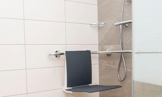 A modern bathroom with a shower and a folding shower seat. The walls are tiled in a bright and friendly manner.