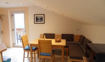 A cozy dining area with a wooden log table and bench. Large windows provide plenty of light in the room.