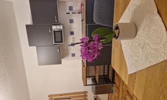 A modern kitchen with gray cabinets and a dining table. On the table sits a purple orchid in a white pot.