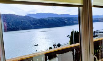 A tranquil lake with gentle waves and mountains in the background. The view is visible through a window with blinds.