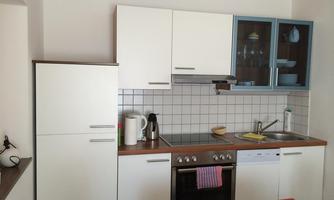 A modern kitchen with white cabinets and a wooden countertop. Visible are a stove, a sink, and various kitchen appliances.