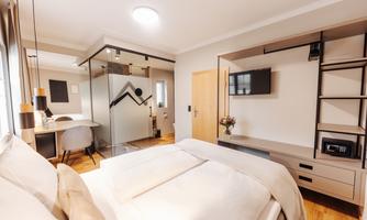 A modern bedroom with a large bed and a stylish wall featuring a television. The room has a workspace and a separate bathroom area.