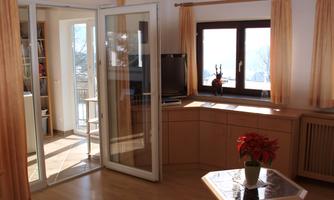 A bright living space with large windows and elegant wooden paneling. A windowsill with a potted plant adds to the cozy atmosphere.