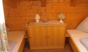 A cozy room with wooden paneling and two single beds. On a table, there is a lamp and a decorative bowl.