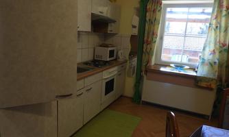 A bright kitchen with modern appliances and a large window. The floor is made of wood and there is a green carpet as well as colorful curtains.