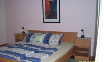 A cozy bedroom with a bed and a colorful blanket. Decorative pictures hang on the walls, and there are nightstands with lamps.