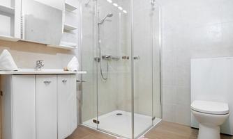 A modern bathroom with a large glass shower and a white toilet. The walls are bright and the furniture is simple and functional.