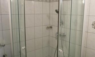 A modern glass shower enclosure in a tiled bathroom. The walls are brightly tiled and the shower is well-lit.