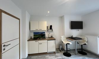 A modern kitchen with a table and two chairs. The walls are painted light and there is a television on the wall.