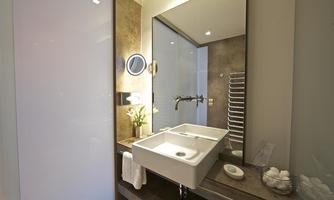 A modern bathroom with an elegant sink and a large mirror. The walls are painted in neutral tones, and a towel rack along with a small plant gives the space a friendly atmosphere.