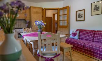 A cozy kitchen with a dining area and a red sofa. A vase with fresh flowers is on the table.