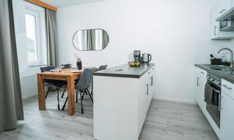 A modern kitchen with a dining table and chairs. The walls are light, and there is a large mirror as well as an attractive countertop.
