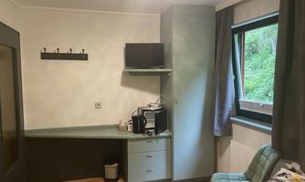 A simple room with a desk, a television, and a chair. Next to the window, the curtains and the wall color are greenish.