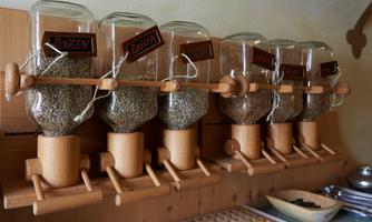 Six transparent containers for storing spices hang on a wooden holder. The containers are labeled.