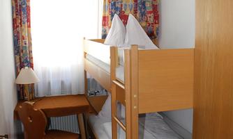 A cozy room with a bunk bed and colorful curtains. There is a small table and a chair for work or relaxation.