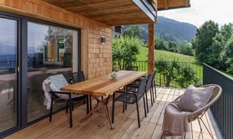 A cozy terrace with a large dining table and chairs. In the background, green meadows and mountains can be seen.