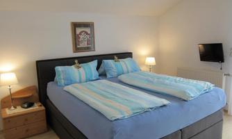 A cozy bedroom with two single beds and blue bed linens. Soft lighting and a television create a relaxing atmosphere.