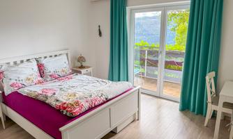 A cozy bedroom with a large bed and colorful bedding. Through the French doors, a beautiful view of nature is visible.