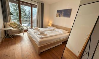 A cozy bedroom with a double bed and a large mirror. The windows offer a view of a snowy landscape.