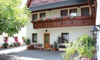 A cozy house with a balcony and blooming plants. The entrance area is bright and welcoming, surrounded by green shrubs.