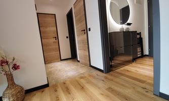 A bright hallway with modern wooden doors and a round mirror. The floor is made of light wood and a decorative plant stands in the corner.