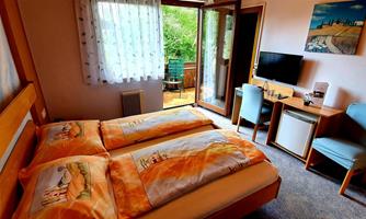A cozy bedroom with two beds and colorful bedding. There is a desk, a television, and access to a balcony with a view of the greenery.
