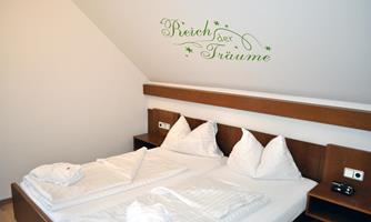 A cozy bedroom with a double bed and white bedcovers. Above the bed is the lettering "Realm of Dreams".