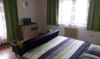 A cozy bedroom with a large bed and colorful stripes on the bedding. Next to the bed, there is a small television and a wooden wardrobe, and the curtains are green.
