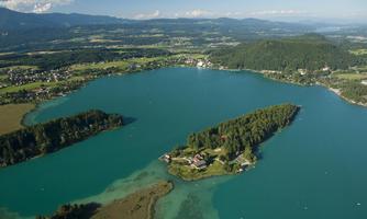 A picturesque lake with clear, blue water. In the background, green hills and a small island with trees can be seen.