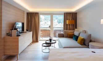 A modern hotel room with a cozy sofa and a view of the mountains. The space is bright and stylishly furnished.