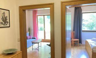 A bright hallway with two open doors. On the left side, you can see a cozy living room, and on the right side, a bedroom.