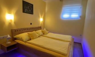 A cozy bedroom with a double bed and yellow pillows. The walls are painted yellow, and there is soft LED lighting under the bed.