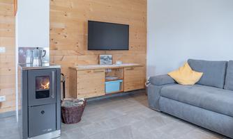A cozy living room with a modern television and wood paneling. A comfortable gray sofa and a fireplace create an inviting atmosphere.