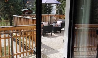 A modern terrace with a view of the mountains and surrounded by trees. There are cozy seating areas outside.