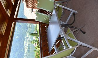 A cozy balcony with a table and four chairs. In the background, there is a beautiful view of a lake and the surrounding mountains.