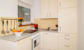 A modern kitchen with bright cabinets and a countertop. In the background, there is a bowl of fresh fruit and a coffee machine is visible.