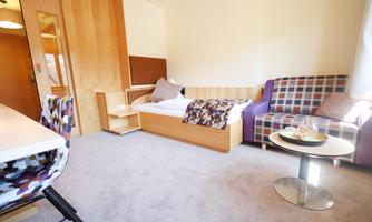 A cozy room with a single bed and a seating area. Bright and modernly furnished, it offers an inviting space to relax.
