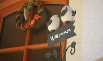 A welcome decoration with two birds and a sign. In the background, a decorative wreath is visible.
