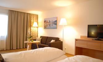 A bright hotel room with two beds and a comfortable seating area. A TV and a picture on the wall complement the decor.