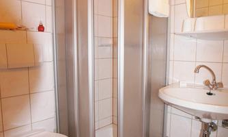 A small bathroom with a shower cabin, a hand wash basin, and a toilet. The walls are tiled, and the decor is simple and functional.